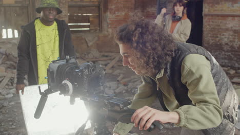 close up view of cameraman setting up a camera in a ruined building while anothers coworkers waiting for start the recording