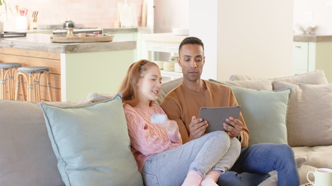 Couple relaxing on sofa, using tablet and credit card for online shopping