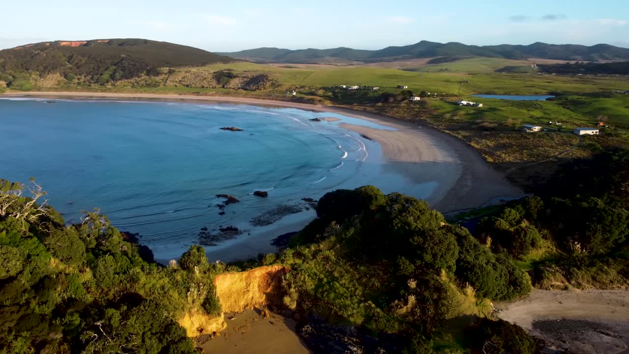 Drone view of beach, bay and grass fields during golden hour sunset at Maitai Bay, Northland, New Zealand.