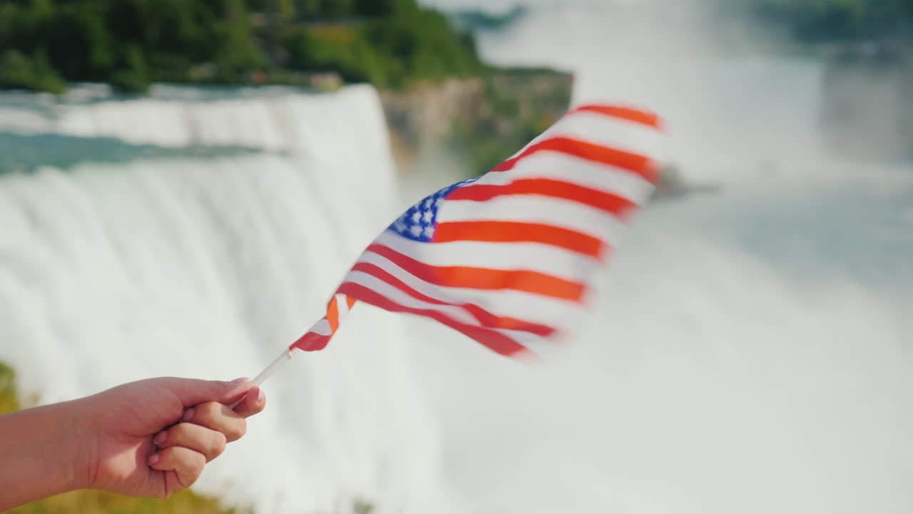 Mano con bandiera USA sullo sfondo delle Cascate del Niagara. Viaggio in America.