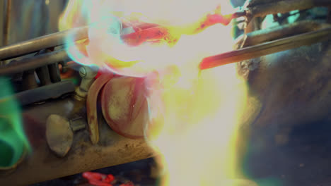 a blacksmith uses gas welding to melt a brass saxophone, resulting in destructive sparks and brightly coloured flames