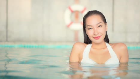 attractive cheerful thai young woman immersed in pool water takes bath with lifebuoy in background