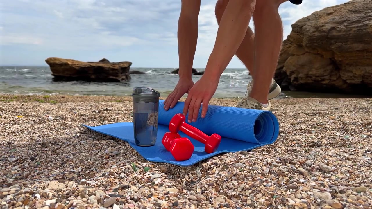 Uomo che srotola il tappetino da yoga sulla spiaggia per allenarsi