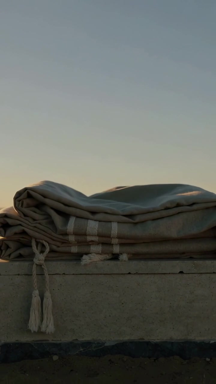 Video verticale: Raffica di vento che solleva una coperta a righe con nappe su una sporgenza all'alba, formando un cappuccio.