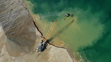 Vista-Aérea-De-Arriba-Hacia-Abajo-De-Una-Excavadora-Que-Mueve-Piedra-Triturada-Al-Agua