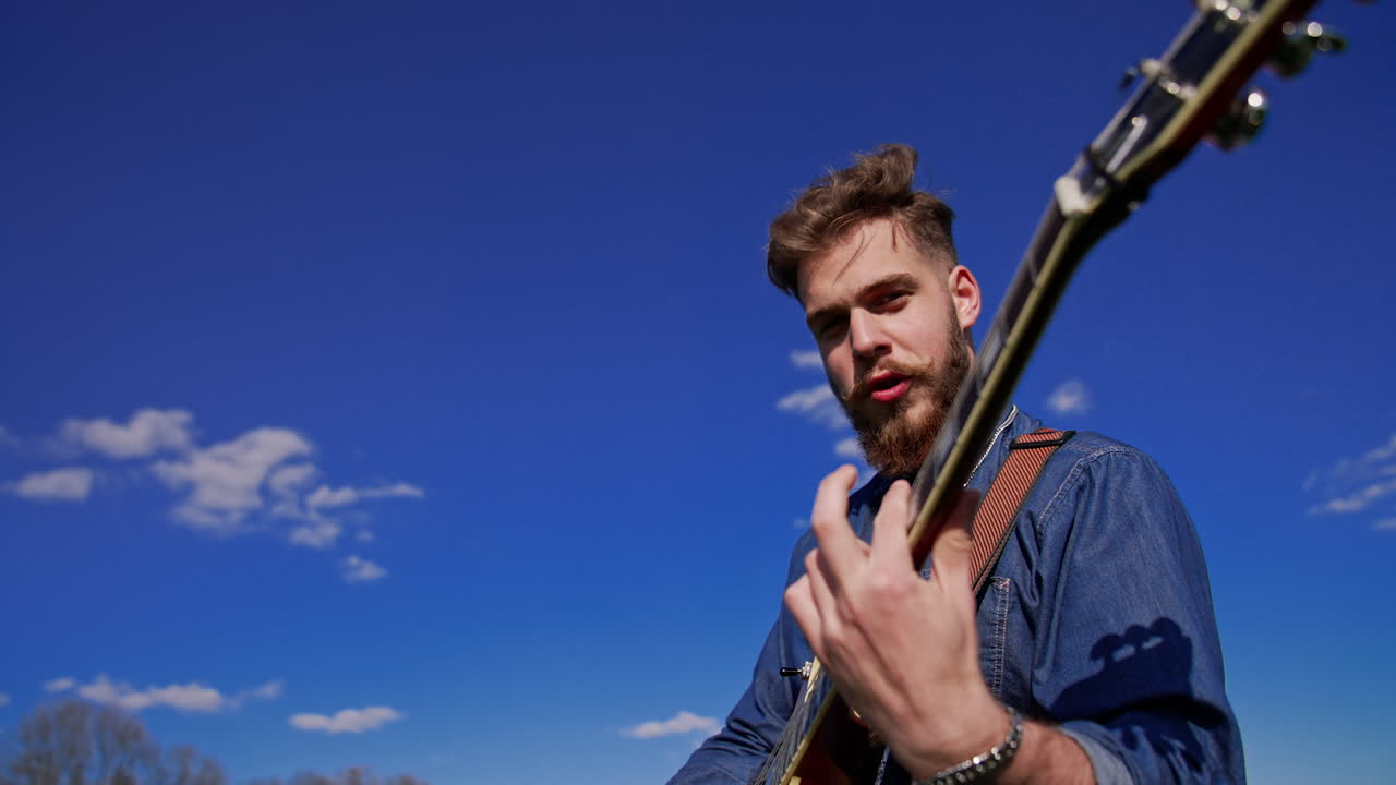 Man playing electric guitar outdoors under a clear sky