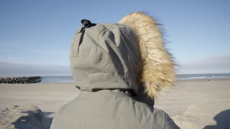 toma panorámica de una persona con abrigo encapuchado mirando y sintiendo la brisa del mar del norte en ostende, bélgica - concepto de atención plena, espíritu, respiración