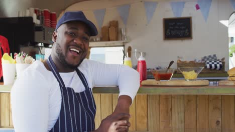 Portrait-of-african-american-man-wearing-apron-smiling-while-standing-near-the-food-truck