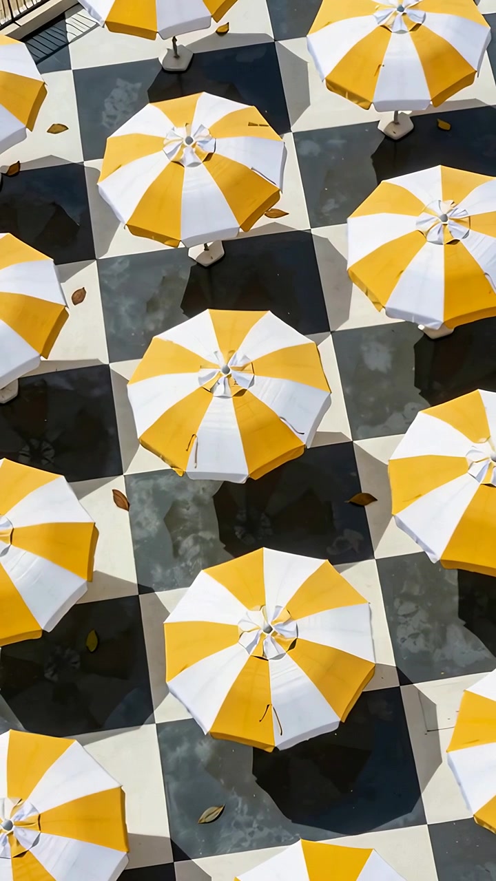 Video verticale: Telecamera in movimento che centra la griglia di un ombrellone a strisce su piastrelle a scacchi, mostrando le ombre.