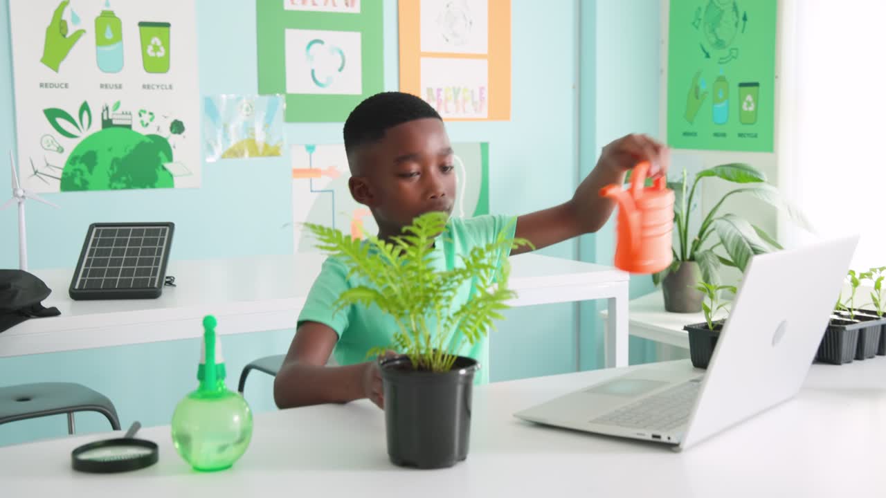 Youth male African American potting sprout from tray into pot, watering and checking laptop in lab