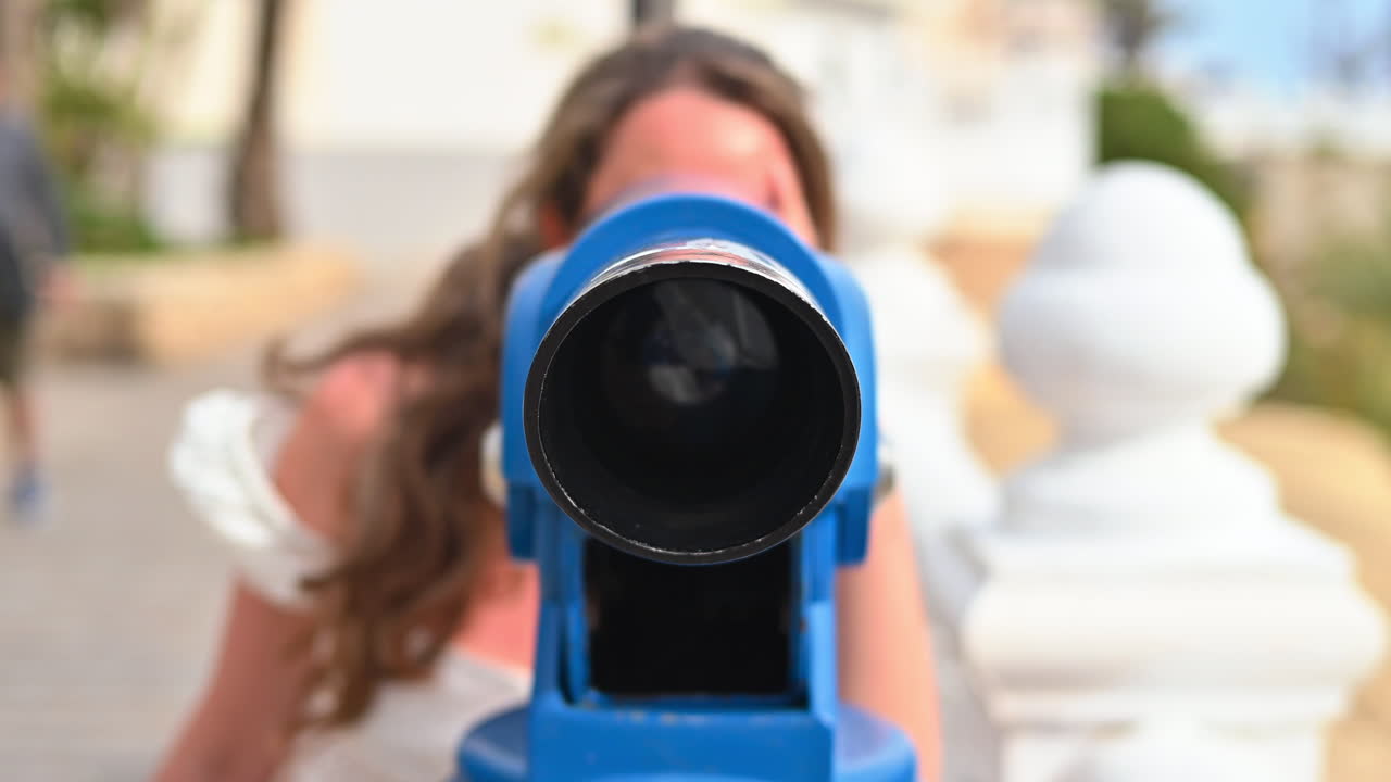 Donna con abito estivo giallo che guarda attraverso un binocolo turistico blu in Spagna