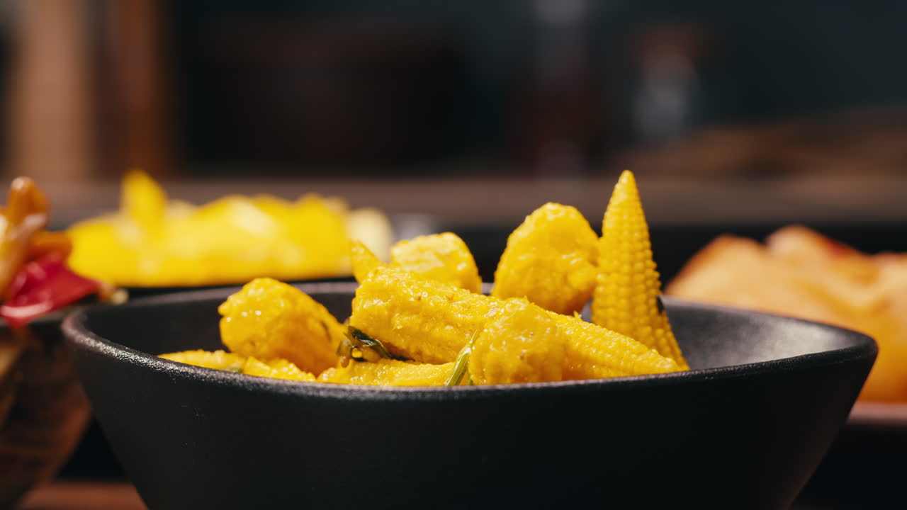 Close-up of fermented yellow mini corn with black pepper on black plate. Preservation of vegetables in glass jars. Fermentation preserved mini corns with spices.