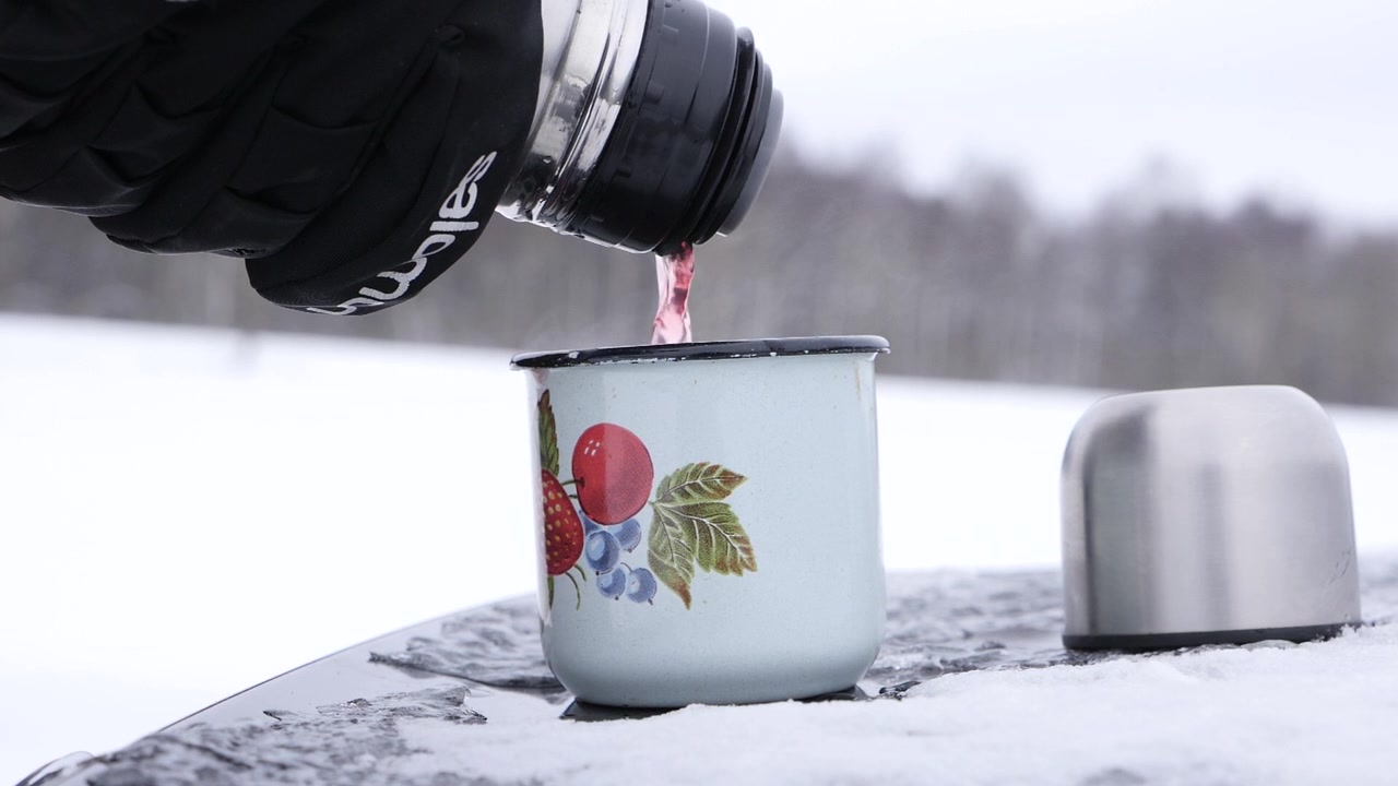 Versare tè caldo nella tazza in inverno, sul retro di un bagagliaio d'auto.