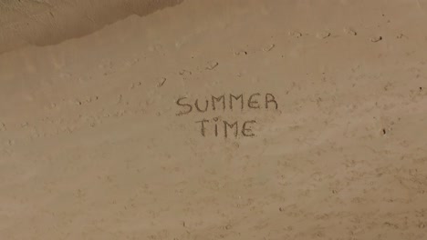 shot with drone from the bottom to the top of the sand and the caribbean ocean, written on the sand "summer time", shot during the day, concept of vacation and fun