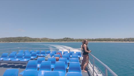 young women staying at the railing of a ferry. looking at tropical islands and taking photos while a boat is leaving