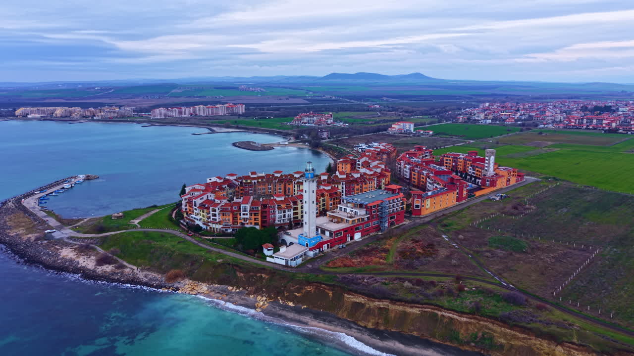 Vista costiera di una città di mare con edifici vicino alla riva e campi verdi sullo sfondo durante una giornata nuvolosa