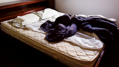 white unmade bed with crumpled messy blanket and pillow in morning light