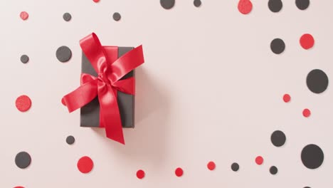 High-angle-view-of-black-gift-box-with-red-ribbon-on-white-with-red-and-black-dots-and-copy-space