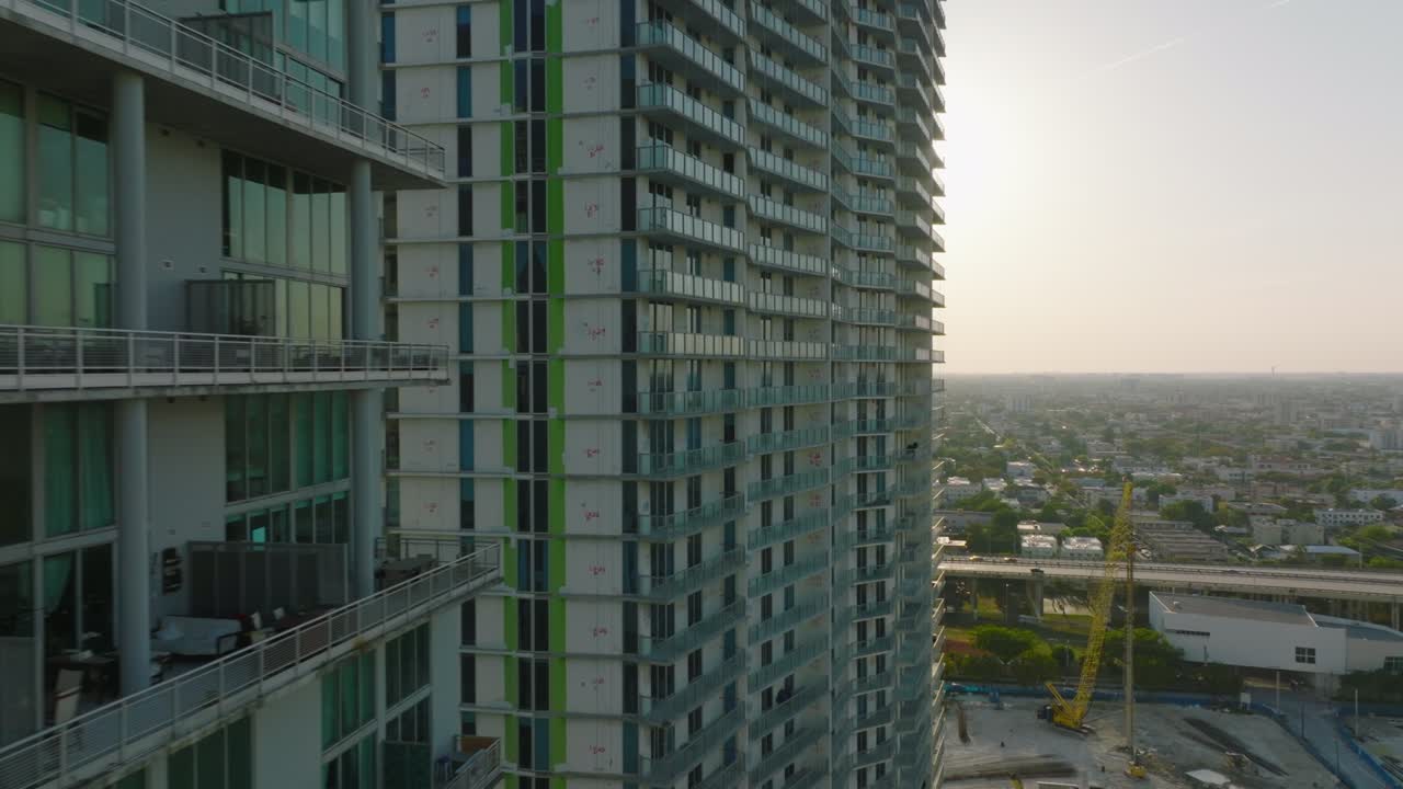 vuelo hacia adelante a lo largo de modernos edificios de apartamentos de gran altura. revelando una gran área plana vista de barrios urbanos residenciales contra el sol. miami, ee.uu.