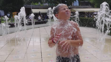 slow motion shot of a boy running through the fountains of a city fountain, during a hot summer day