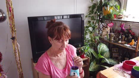 mujer mayor argentina bebiendo mate tradicional sudamericana rica en cafeína infundida bebida a base de hierbas sola en su casa rodeada de plantas verdes