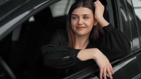 Hübsche-Junge-Frau,-Die-Hinter-Dem-Rad-Eines-Neuen-Autos-Sitzt,-Glättet-Ihr-Haar-Und-Lächelt