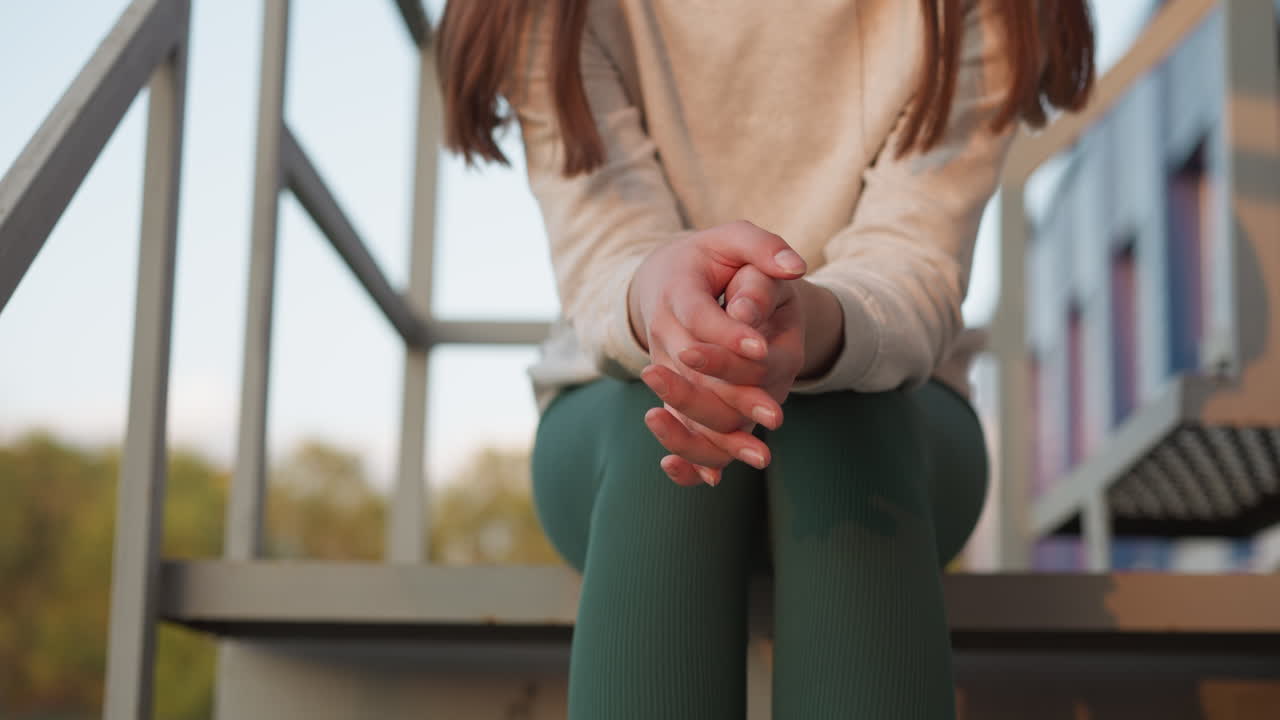 mujer se sienta con los dedos cruzados en las escaleras. mujer joven se siente nerviosa acerca de los eventos futuros mientras pasa tiempo a solas. estado nervioso y deprimido