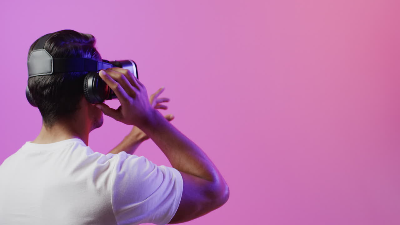 video de un hombre biracial usando auriculares vr en un fondo rosa y púrpura