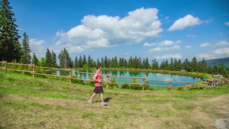 Adult-Male-Jogging-Downhill-Past-Beautiful-Lake-In-Kope,-Slovenia