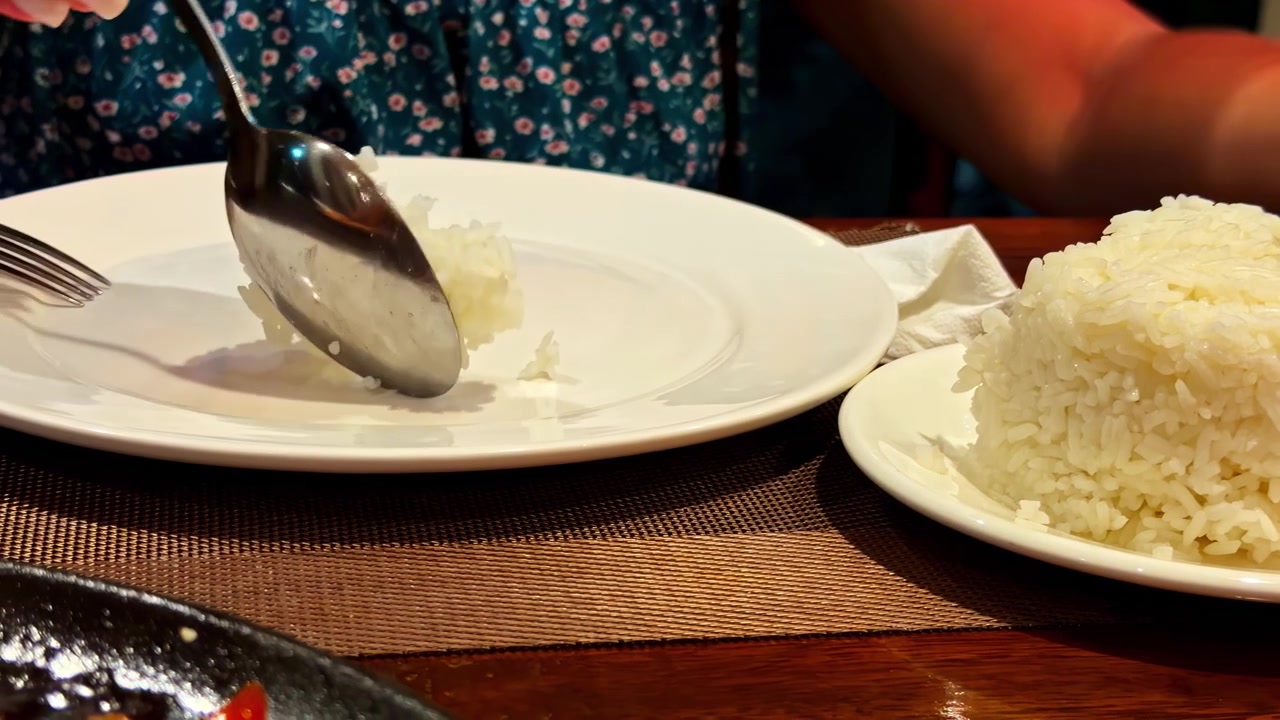 Close-up view of plates of steamed rice and other simple dishes on a wooden table, likely at a casual eatery in the Philippines