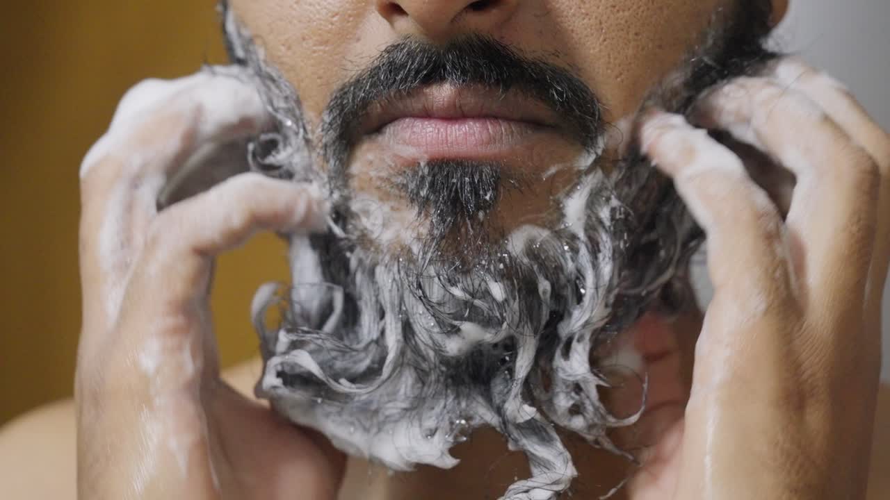 A close-up footage of a South Asian man rubbing his beard with soap and water, with a blurred background