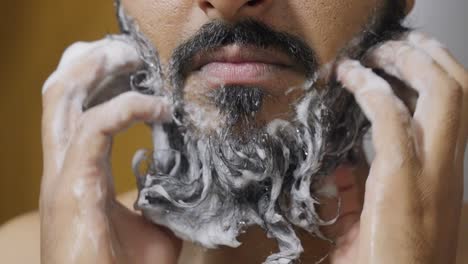 a close-up footage of a south asian man rubbing his beard with soap and water, with a blurred background