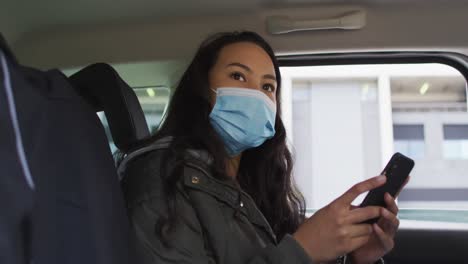 Asiatische-Frau-Trägt-Gesichtsmaske-Und-Benutzt-Smartphone,-Während-Sie-Im-Auto-Sitzt