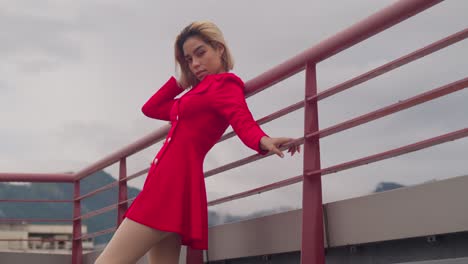 In-Port-of-Spain,-Trinidad,-a-young-girl-of-Hispanic-descent-stands-on-a-rooftop,-dressed-in-red,-with-cloudy-skies-in-the-distance-low-angle