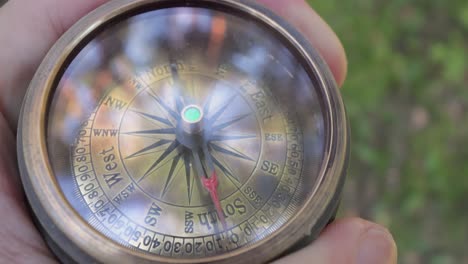 Traveler-hand-holds-a-old-directional-compass-in-summer-forest.-Person-use-compass-to-find-location.-Travel-concept-close-up.