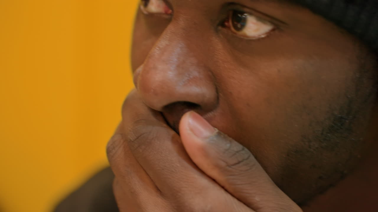 Uomo che si strofina gli occhi mentre ascolta con le cuffie. Primo piano di un cantautore pensieroso, con uno sfondo giallo da studio. Pausa riflessiva e stanchezza, ritratto intimo, luce calda e soffusa, introspezione creativa.