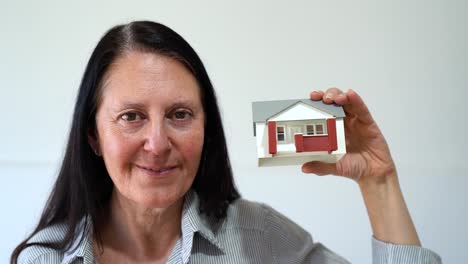 smiling woman holds miniature model of house. real estate investment concept. closeup shot