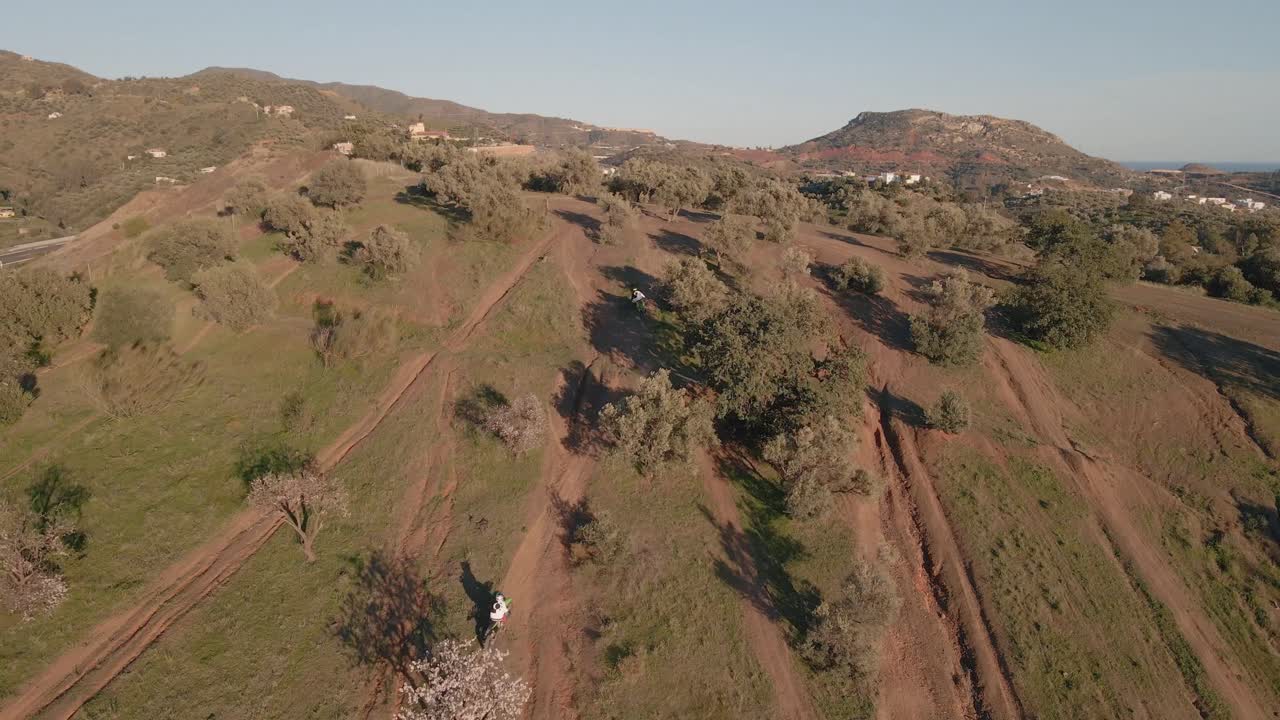 화창한 날 오토바이 운전자들이 경주를 하는 동안 나무, 먼지투성이 트랙, 언덕이 있는 말라가 스페인의 산에 있는 모터크로스 트랙의 공중 와이드 돌리 샷