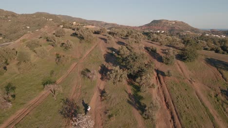 Aerial-wide-dolly-shot-of-a-motorcross-track-on-a-mountain-in-Malaga-Spain-with-trees,-dusty-track-and-hill-while-motorcyclists-are-racing-on-a-sunny-day