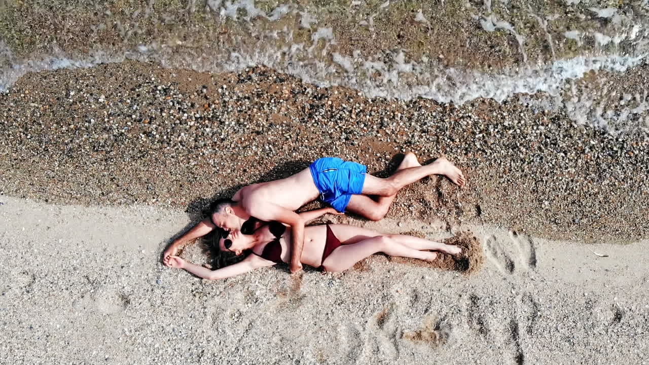 Top view of mature couple sitting the beach near water hugging and kissing