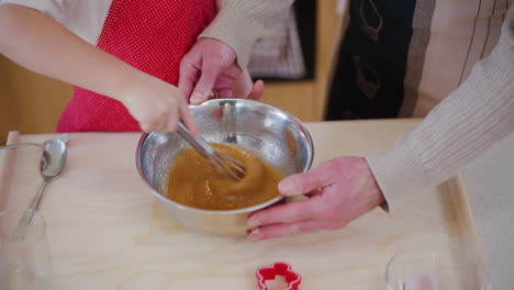 young boy helps dad beat eggs in metal bowl while preparing food