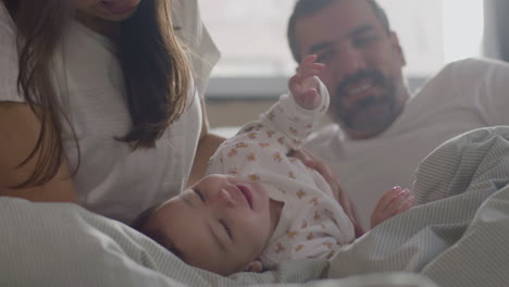 mittlere aufnahme einer glücklichen mutter, die ihre kleine tochter kuschelt und kitzelt, während papa sie beobachtet und lächelt