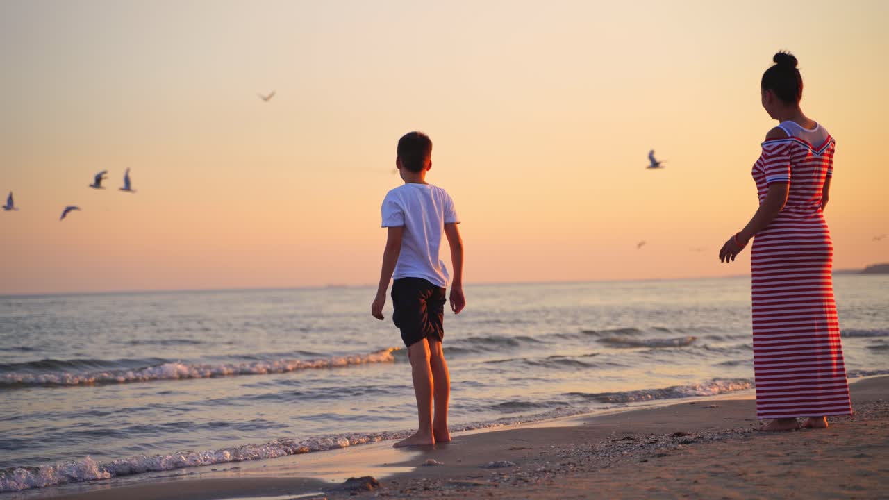 Cute boy and woman near the sea at sunset. Mother and her son having fun together on the evening sea water background.