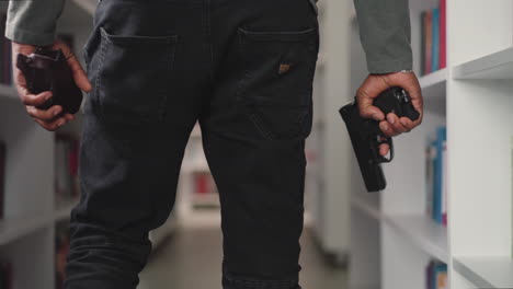 policeman with gun walks along aisle in public library closeup. security guy protects store with handgun. african american man prevents crime