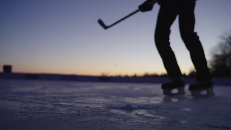 slow motion, silhouette of ice hockey player stopping in front of camera in outdoor ice rink