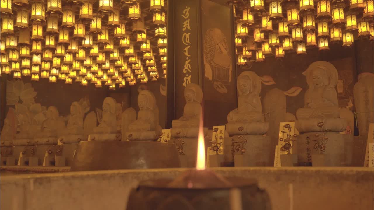 Rows of Buddha statues illuminated by hundreds of golden lanterns in a tranquil temple on Miyajima Island, Japan.
