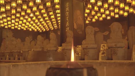 rows of buddha statues illuminated by hundreds of golden lanterns in a tranquil temple on miyajima island, japan.