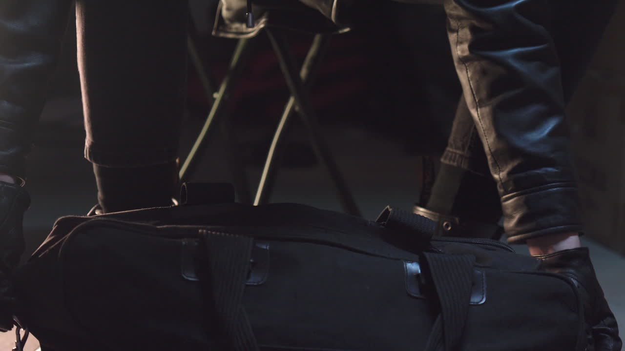 criminal con guantes de cuero cerrando una bolsa de lona negra y alejándose