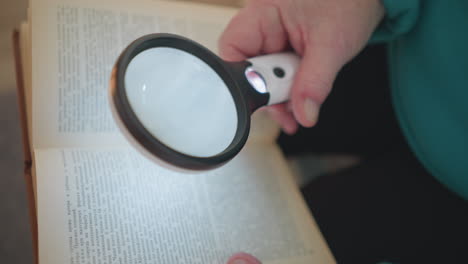 close-up view of elderly woman holding magnifying glass, reading large text in book. soft lighting highlights details in book, with focus on magnifier as she examines text. focused, curious expression