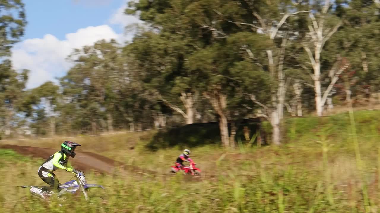 A motorcyclist skillfully rides through a winding dirt path surrounded by lush greenery and tall trees.